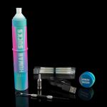 A colorful, cylindrical cannabis dab rig with accompanying tools, cartridges, and a charging cable, displayed on a reflective surface.