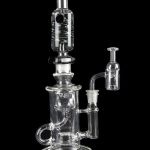 Clear glass water pipe (rig) with multiple chambers and a separate oil dome, isolated on a black background.