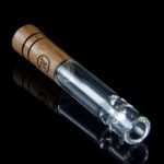 Glass pipe with wooden mouthpiece on a reflective surface.