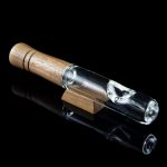 Glass bubbler pipe with a wooden mouthpiece, reflecting on a glossy black surface.