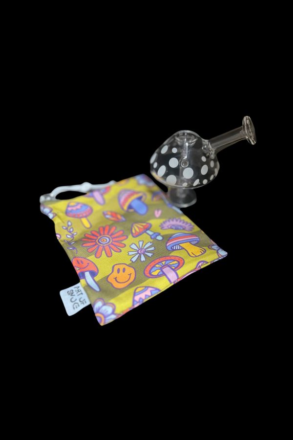 A glass bubbler pipe rests beside a colorful, patterned draw string bag featuring psychedelic floral and mushroom designs.