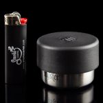Black cannabis storage jar and lighter with branding for Smoke Cartel, reflecting on a glossy surface.