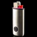 Silver cannabis grinder with a lighter inserted into the top, reflecting on a black surface.