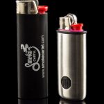 Two butane lighters with branding for Smoke Cartel, displayed on a reflective black surface.