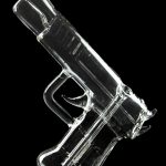 Clear glass pipe shaped like a handgun, reflecting on a dark surface.