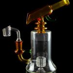 A clear glass dab rig with orange accents, featuring a perc diffuser and separate nail, isolated on a black background.