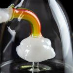 A close-up of a glass cannabis oil rig with a white and colorful mouthpiece, set against a dark background.