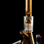 Glass water pipe (bong) with detached glass pieces and lighter against a black reflective surface.