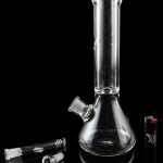 Glass bong and accessories on a reflective surface.