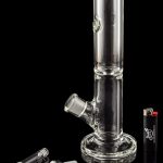 Clear glass water pipe (bong) with detached glass bowls and a lighter on a reflective surface.