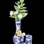 Blue and white porcelain cannabis vase with ferns and a matching jar and saucer set, isolated on a black background.