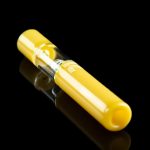 Yellow glass cannabis oil burner pipe with a clear glass bubble, reflecting on a black surface.