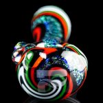 Hand-blown glass cannabis water pipe with vibrant swirling colors and glitter accents, reflecting on a dark surface.