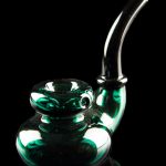 Emerald green glass bubbler with intricate swirls, reflecting on a dark surface.