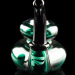 Green and black glass dab rig with reflective surface, isolated on black.