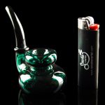 Green glass bubbler pipe and lighter against a black reflective surface.