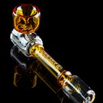 Glass cannabis pipe with orange and clear glass, reflected on a black surface.