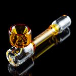 A vibrant orange and clear glass pipe with a bulbous bowl, reflected on a dark surface.