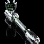 Clear glass cannabis oil rig with green accents, displayed on a reflective black surface.