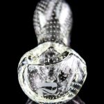 Clear glass cannabis oil rig with intricate bubble and swirl patterns, reflected on a black surface.