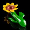 Hand-blown glass pipe shaped like a blooming flower with green stem and leaves, isolated on a black background.