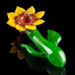 Hand-blown glass pipe shaped like a blooming flower with green stem and leaves, isolated on a black background.