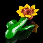 Hand-blown glass cannabis water pipe shaped like a blooming flower with green leaf accents, isolated on a black background.
