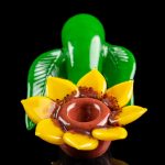 A vibrant glass sculpture resembling a lotus flower with a built-in bowl, set against a black background.