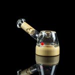 Glass cannabis oil rig with a wooden base and clear glass mouthpiece, reflected on a black surface.