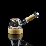 A glass bubbler pipe with a wood-grain patterned mouthpiece, displayed against a black reflective surface.