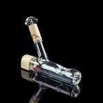 Glass bubbler with intricate internal design and cork accents, isolated on a black reflective surface.