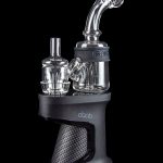 A close-up, angled view of the Ispire Daab E-Rig featuring a dark-colored base and a clear glass bubbler attachment.