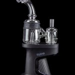 A black “Inspire” branded cannabis oil rig with glass water pipes and attachments, isolated on a black background.