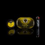 Product shot of Honeybee Herbs cannabis tins and rolling paper packaging on a reflective black surface.