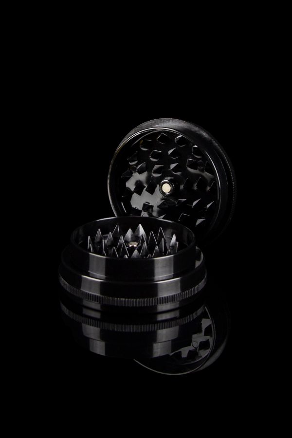Black metal cannabis grinder disassembled, revealing tiered grinding components.