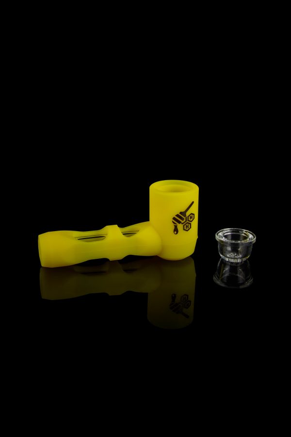 Yellow glass pipe and small cannabis concentrate container on a reflective black surface.
