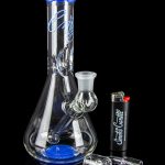 Blue glass water pipe with cannabis accessories on a reflective surface.