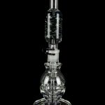 Clear glass water pipe (rig) with intricate bubble and cylinder design, reflecting on a black surface.