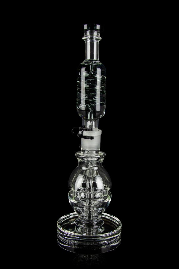 Clear glass water pipe (rig) with intricate bubble and cylinder design, reflecting on a black surface.