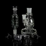 Clear glass dab rigs and accessories displayed on a reflective black surface.
