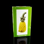Retail packaging for a yellow ceramic pineapple-shaped cannabis pipe, reflected on a glossy surface.
