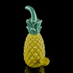 A glass pineapple-shaped water pipe with a green stem and base, reflected on a black surface.