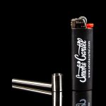 Black lighter and metal smoking pipe on a reflective surface, branded with "Smoke Cartel" logo.