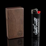 Dark wood cannabis storage box with engraved design next to a lighter branded with “Smoke Cartel” logo, reflected on a black surface.