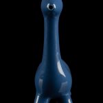 Blue glass water pipe shaped like a giraffe with gold horns, reflected on a black surface.