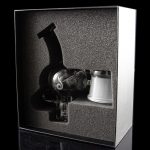 A cannabis dab rig and accessories displayed in a sleek, black presentation box with a reflective surface.
