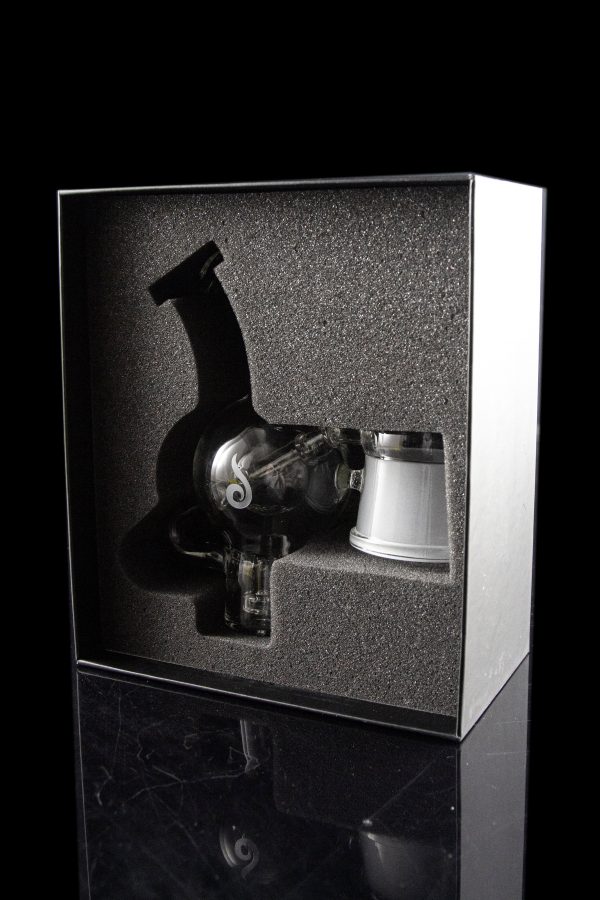 A cannabis dab rig and accessories displayed in a sleek, black presentation box with a reflective surface.