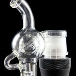 Clear glass water pipe (rig) with a skull-shaped bubbler attached to a black electronic heating device, isolated on a black background.