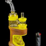 Brown electronic dab rig with glass water pipe attachment and lighter, reflecting on a glossy surface.