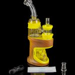 Yellow cannabis concentrate vaporizer (dab rig) with glass attachments and accessories on a reflective surface.